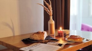 A wooden table with a loaf of bread, a candle, a vase with dried plants, and a menu.