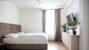 A bedroom with a bed, a nightstand, a dresser, a TV, and a window with curtains.