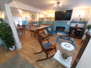 A spacious living area with a dining table, a blue sofa, a TV, and a fireplace. - Torbay Guesthouse (Paignton)
