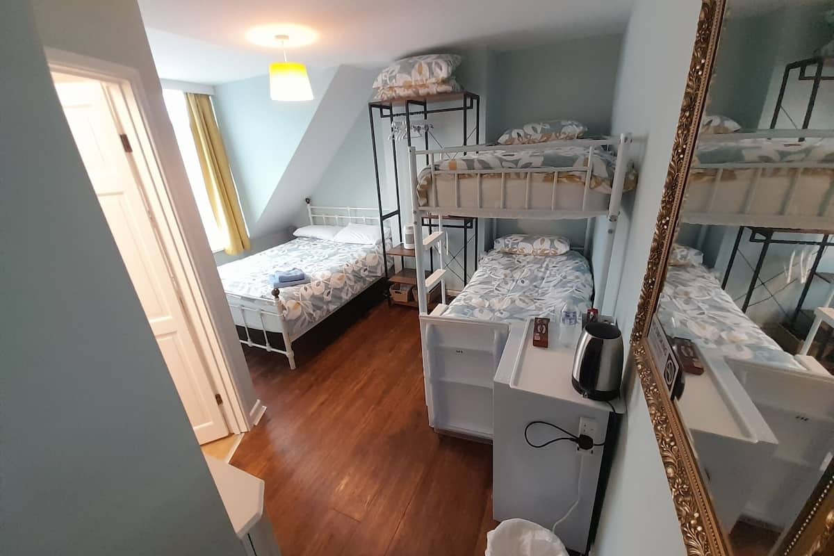 A dormitory room with bunk beds, a desk with a kettle, and a mirror.