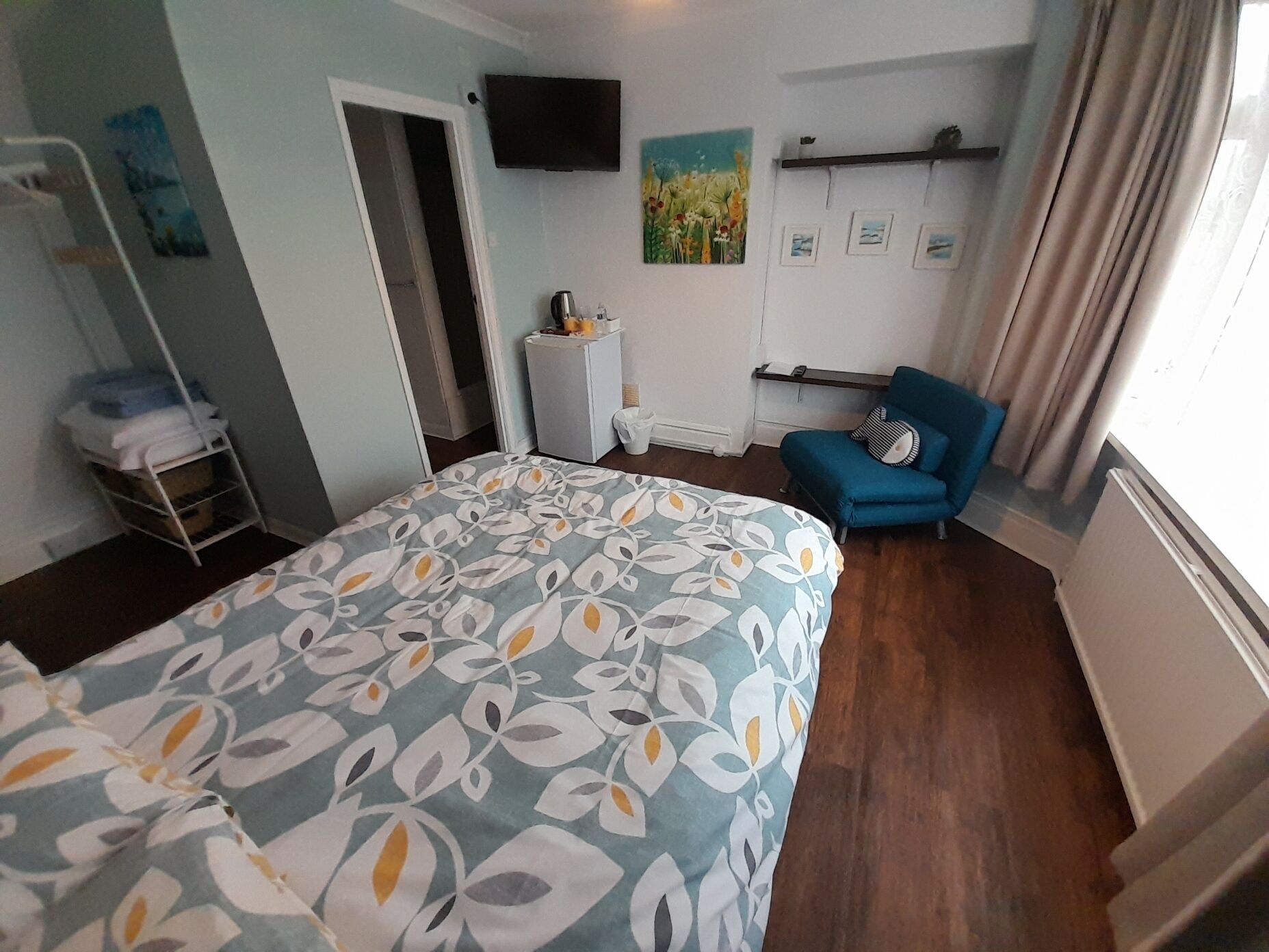 A hotel room with a bed, a chair, a TV, and a window with curtains.