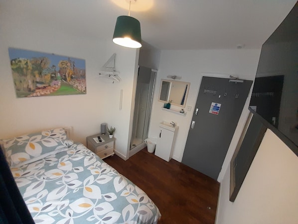 A bedroom with a bed, bedside table, nightstand, dresser, mirror, and a door with a sign. - Torbay Guesthouse (Paignton)