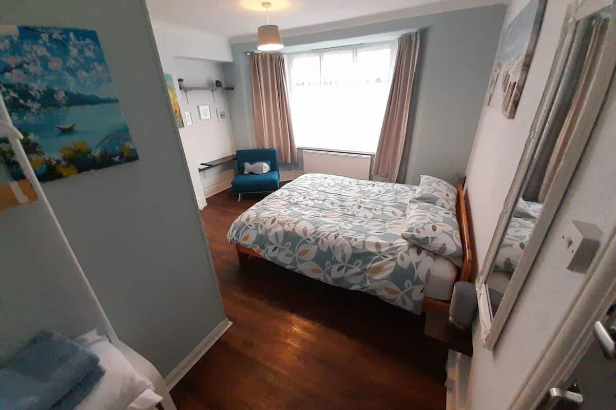 A bedroom with a bed, a chair, a painting, and a window with curtains.