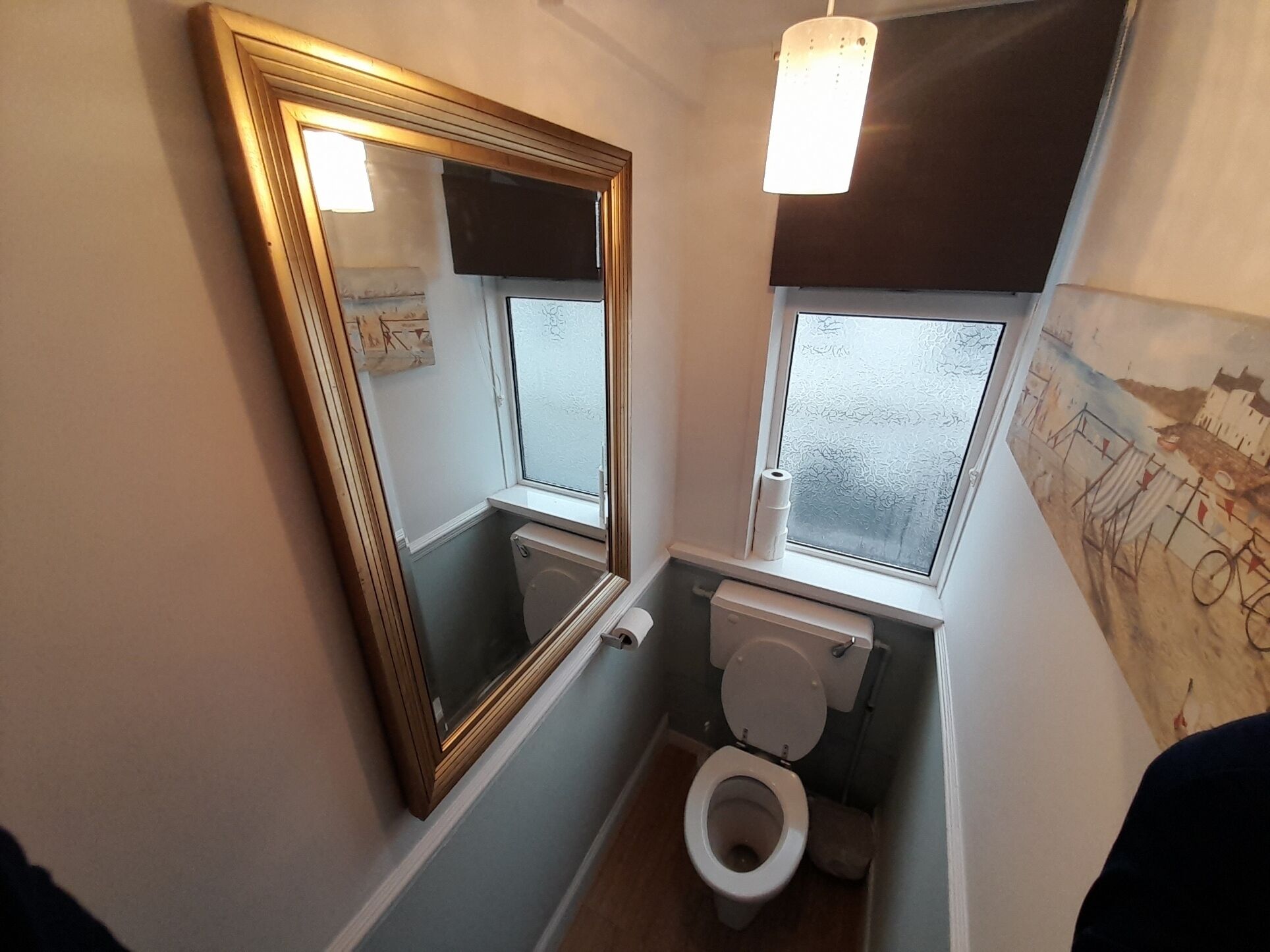 A small bathroom with a toilet, a window, and a mirror.