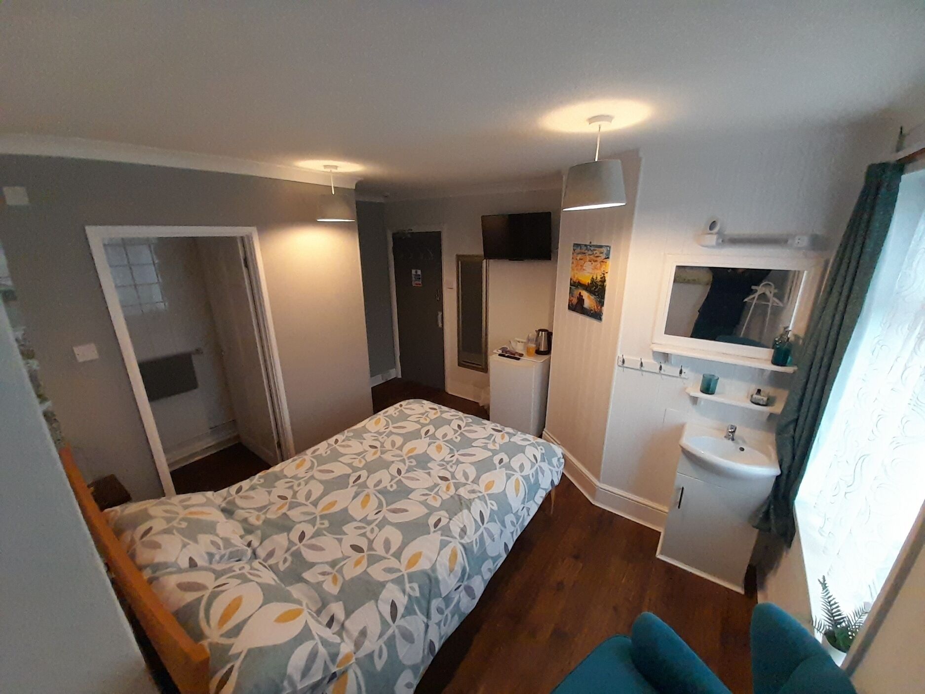 A compact room with a bed, a small kitchenette, a bathroom, and a window with curtains.