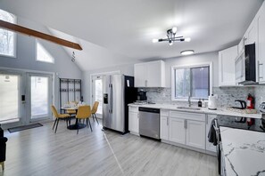 Une cuisine moderne avec des meubles blancs, un réfrigérateur en acier inoxydable, un lave-vaisselle et un coin repas avec des chaises jaunes.