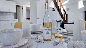 A dining table set with white plates, bowls, and cutlery, a bottle of Blue Ridge wine, and a glass of wine. - The Cozy Modern Cabin – Ski & Relax (Tobyhanna)