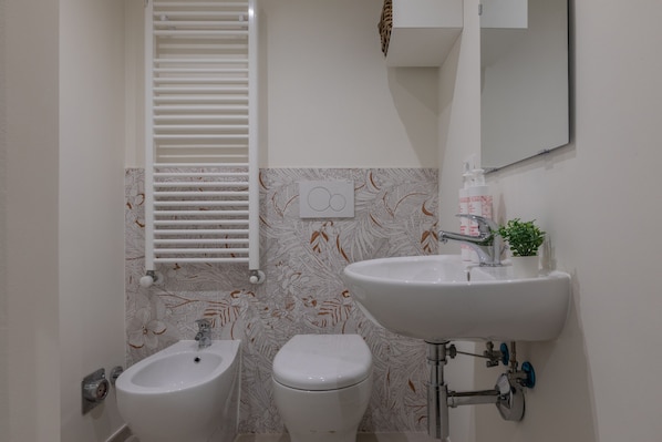 A bathroom with a bidet, toilet, sink, and a towel rack.