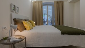 Camera da letto ordinata con un letto, un comodino con una lampada, una piccola pianta e una finestra con tende.