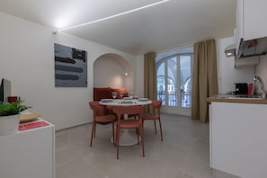 A modern dining area with a round table and chairs, a kitchen with a sink and stove, and a large window with curtains.