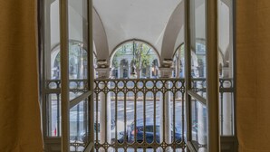 Vista attraverso una finestra con inferriate decorate, che mostra una strada con auto parcheggiate e edifici sullo sfondo.