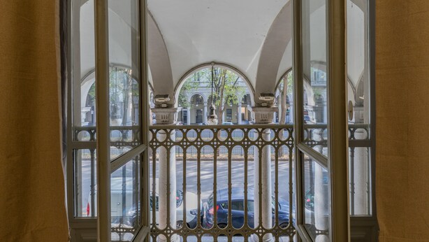 A view through a window with ornate metal bars, revealing a street with parked cars and buildings in the background. - Ai Portici di Susa - Classy by Wonderful Italy (Turin)