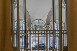 A view through a window with ornate metal bars, revealing a street with parked cars and buildings in the background.