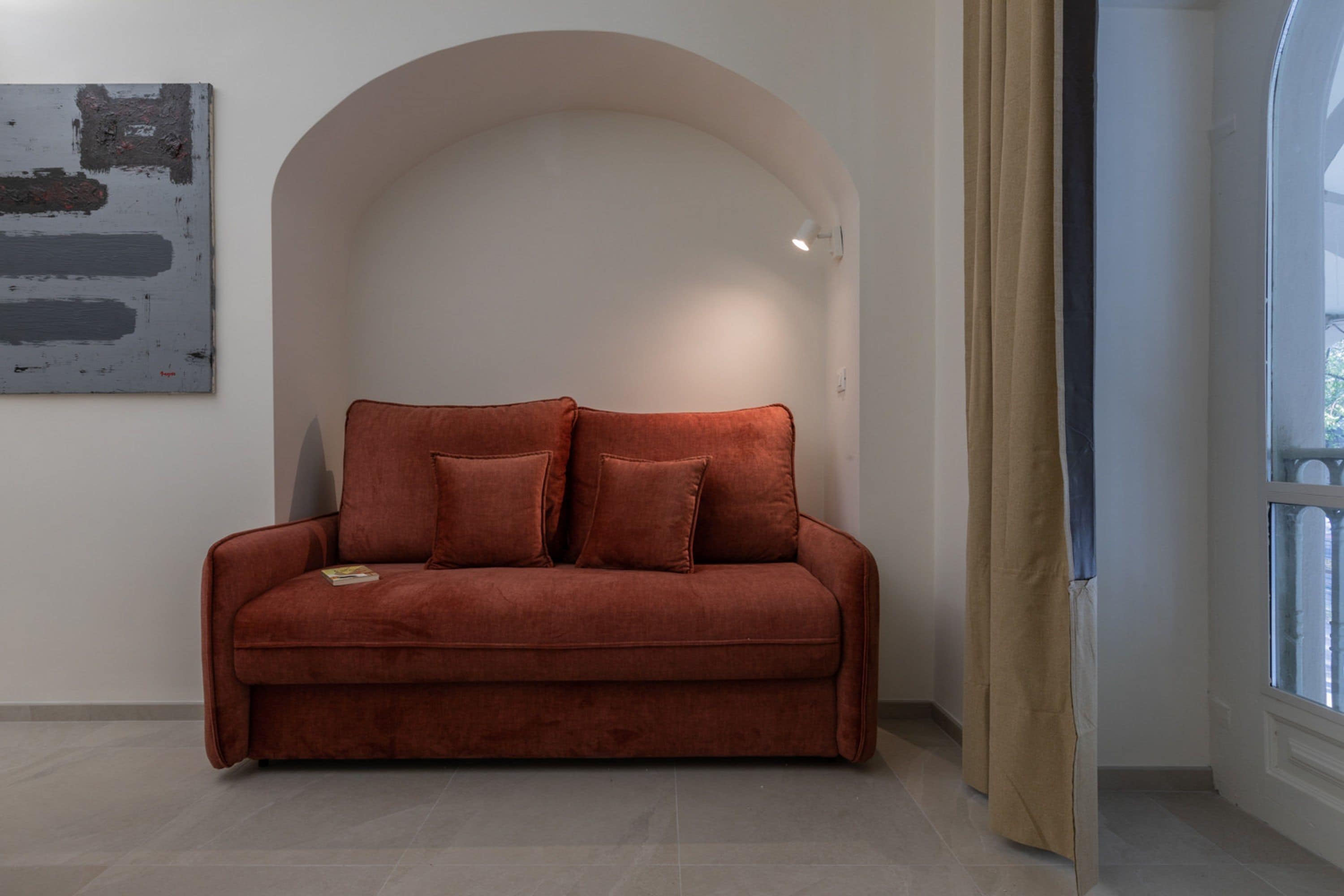Un sofá rojo en una habitación con pared blanca y un ventanal grande.