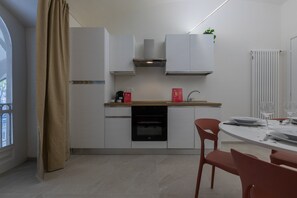 A modern kitchen with white cabinets, a black oven, and a dining area with a round table and red chairs. - Ai Portici di Susa - Classy by Wonderful Italy (Turin)