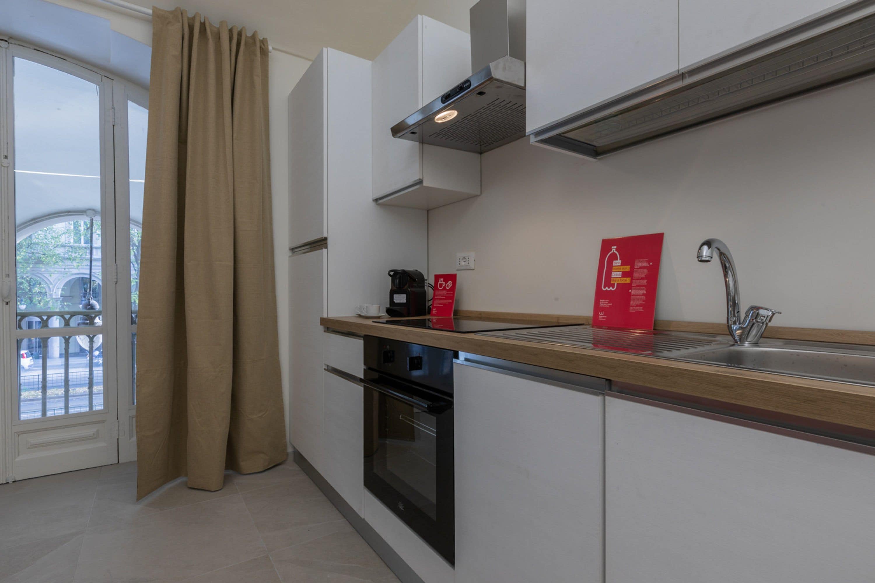 Una cocina moderna con horno empotrado, pileta de acero inoxidable y un cartel informativo rojo.