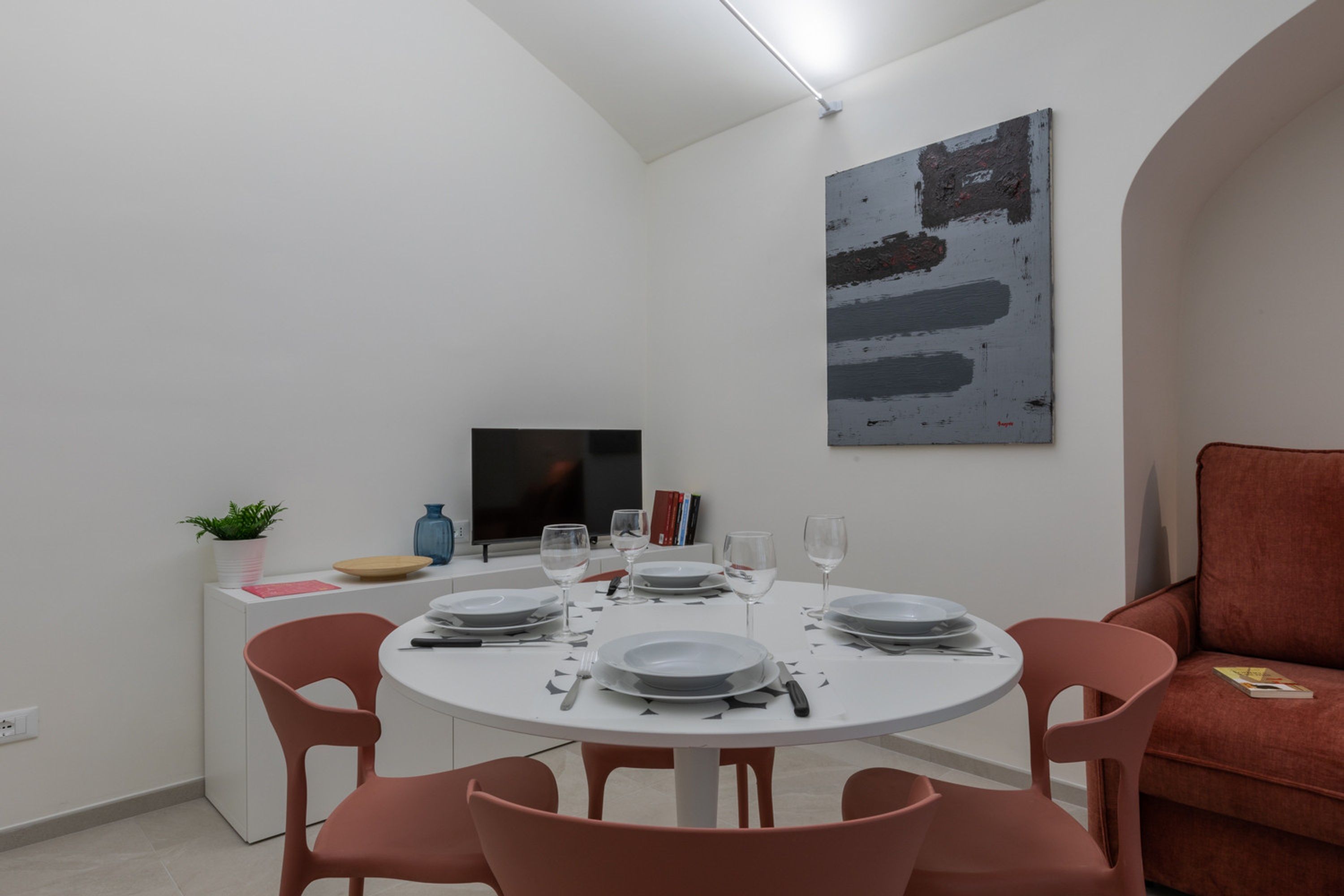 A dining area with a round table set for four, surrounded by pink chairs. A flat-screen TV is mounted on the wall above the table.