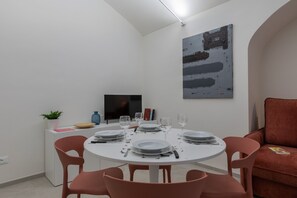 A dining area with a round table set for four, surrounded by pink chairs. A flat-screen TV is mounted on the wall above the table. - Ai Portici di Susa - Classy by Wonderful Italy (Turin)