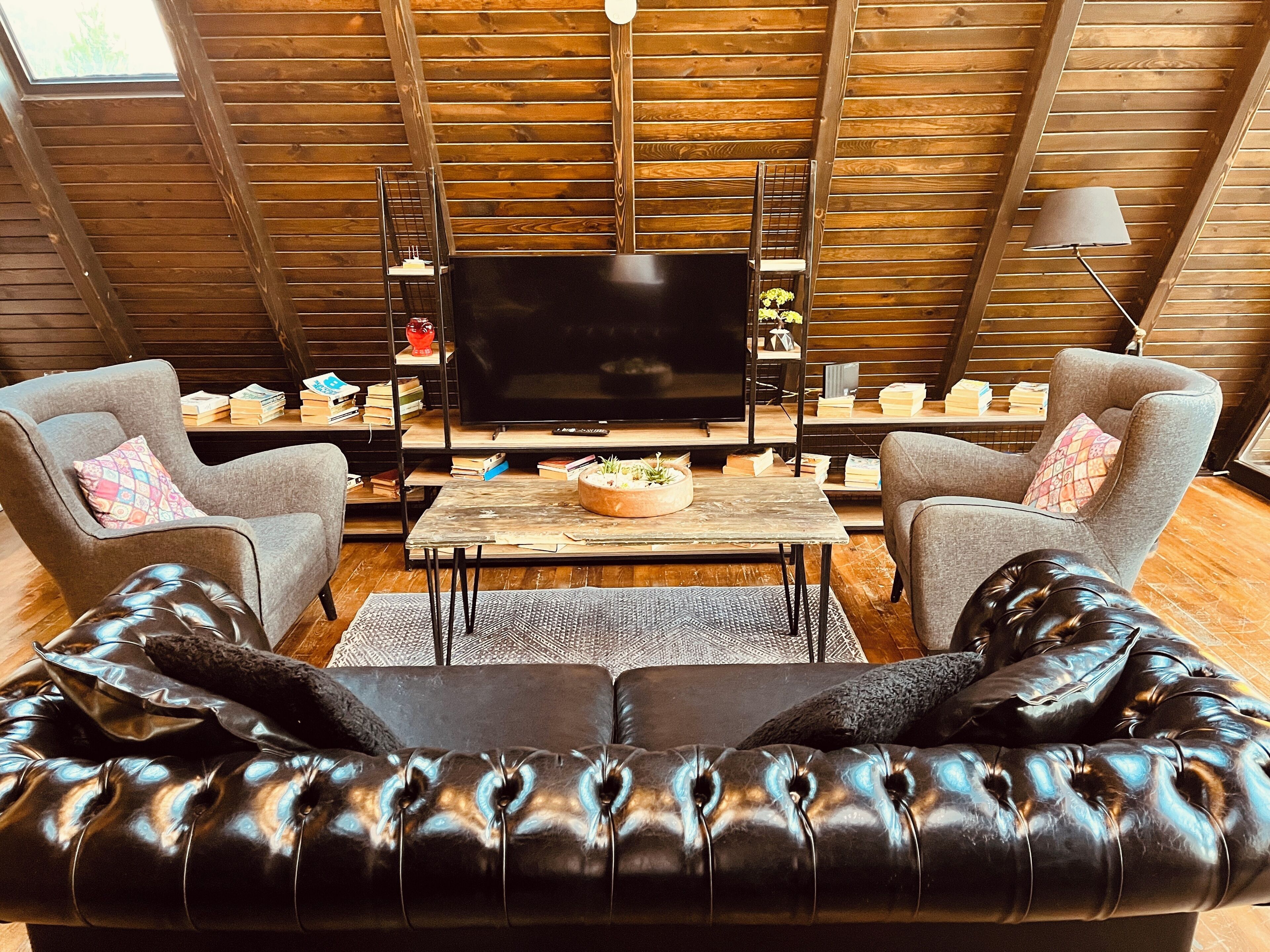 Una sala de estar estilo loft acogedora, con un televisor de pantalla plana grande, sofás de cuero y techo de madera.