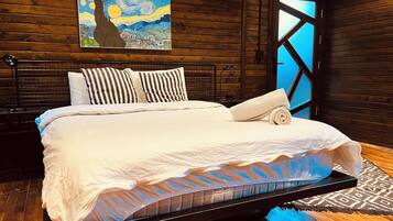 Un dormitorio moderno con cabecera de madera, un cuadro grande sobre la cama y vistas a través de una ventana de diseño geométrico.