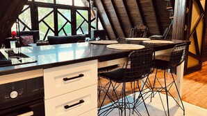 A modern kitchen with a black countertop, white drawers, and black chairs. -  Otelox Sinap Bungalow  (Erdemli)