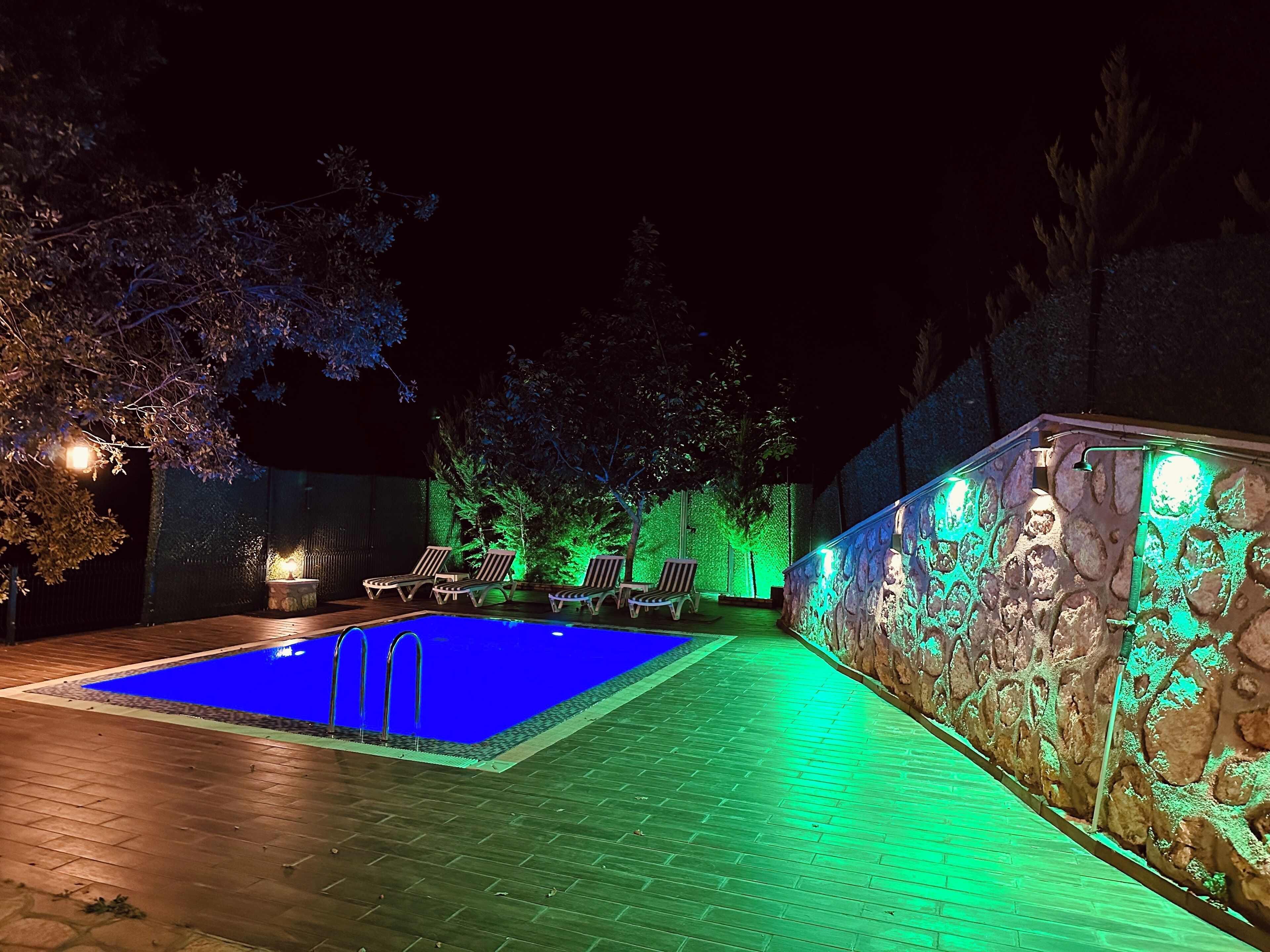 A nighttime swimming pool area with a stone wall and green lighting.