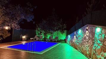 A nighttime swimming pool area with a stone wall and green lighting.
