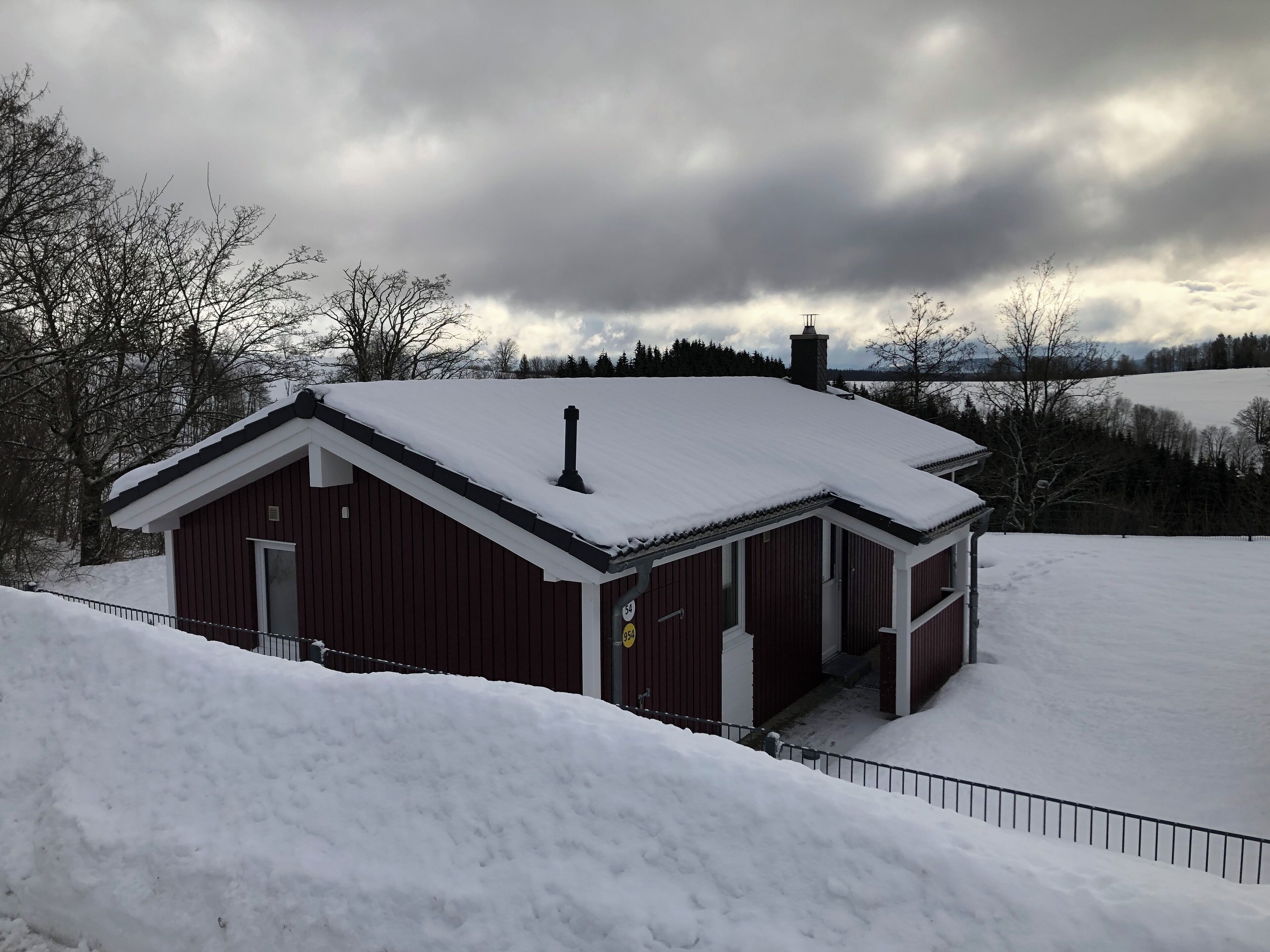A red wooden cabin with a snow-covered roof and chimney, surrounded by a snow-covered landscape.