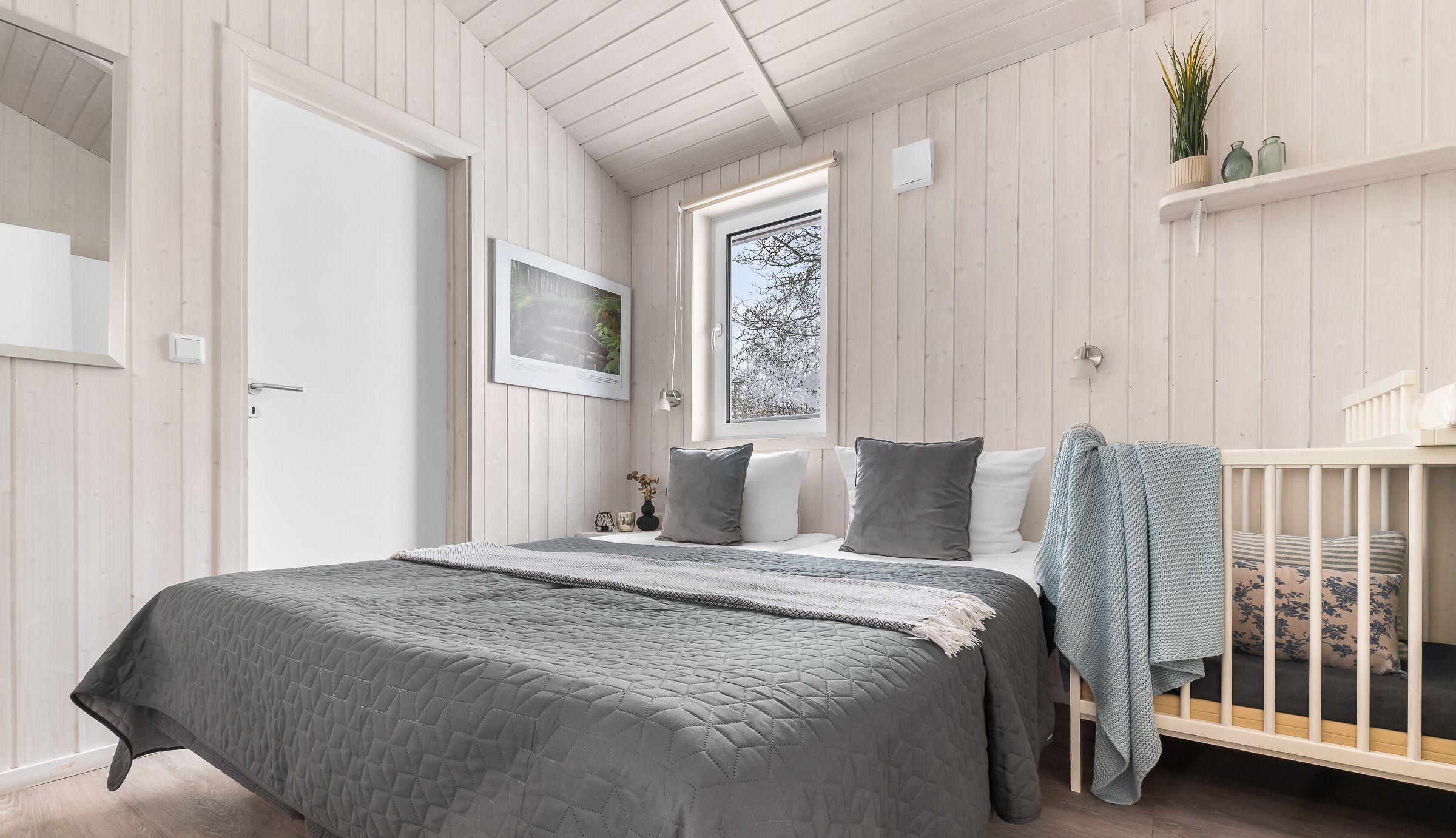 A bedroom with a bed, a crib, a window, and a shelf with plants.