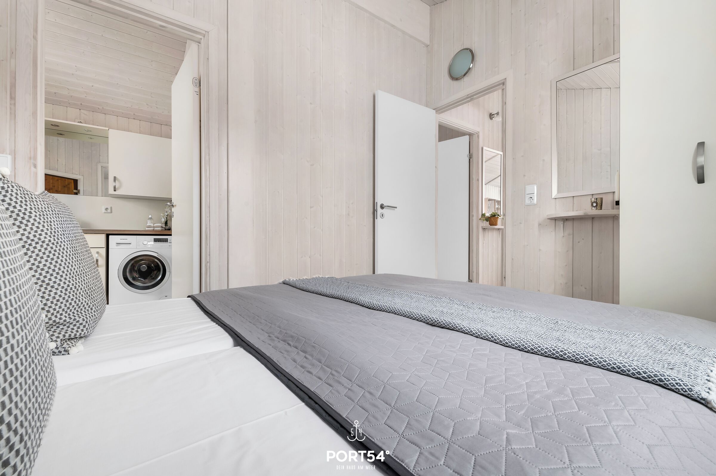 A modern bedroom with a bed, a washing machine, and a mirror.