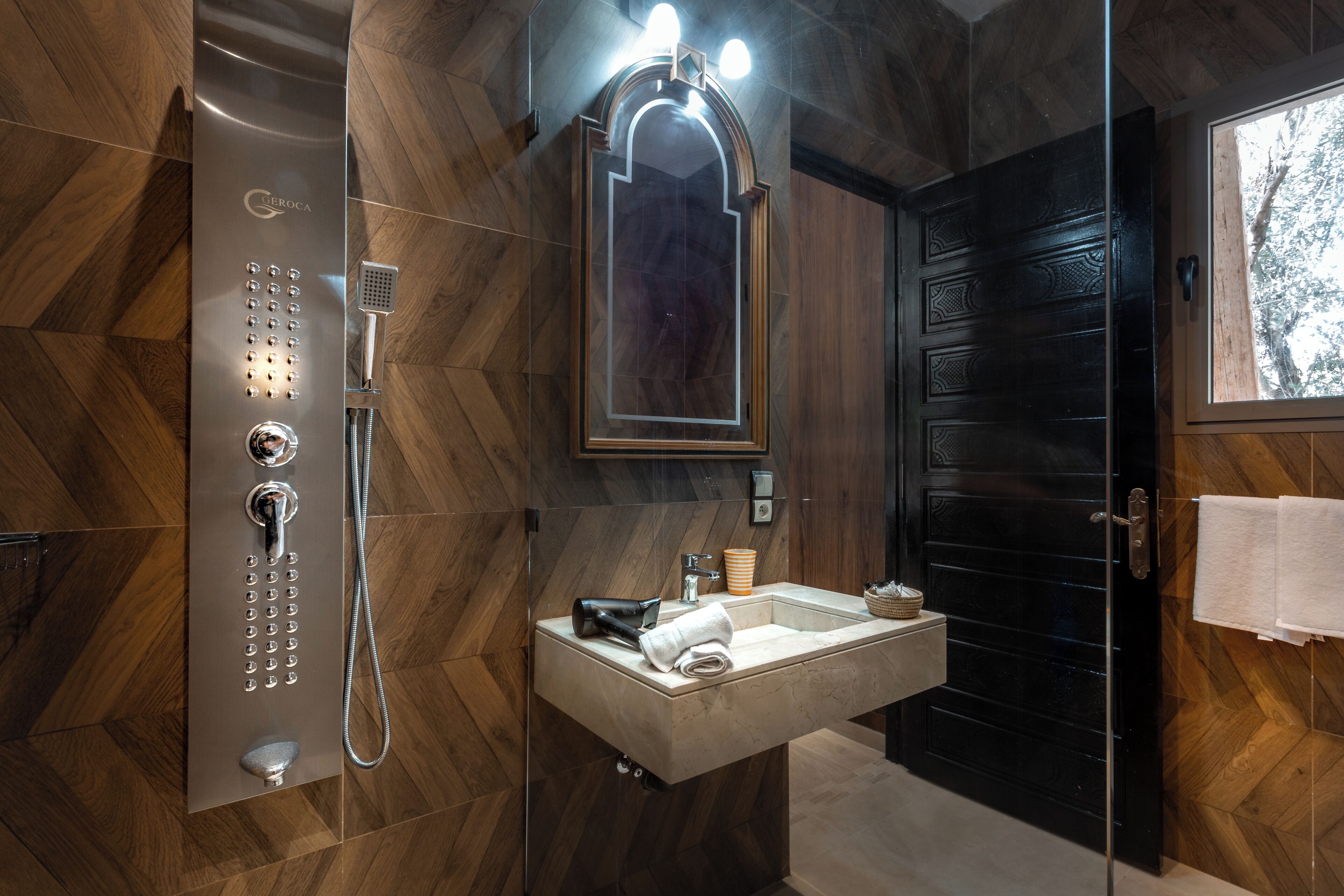 Un baño moderno con ducha integrada, tocador con espejo y puerta de madera oscura.