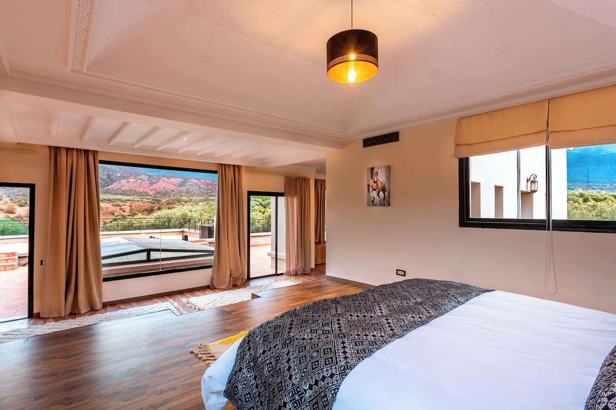 Ein geräumiges Schlafzimmer mit einem großen Bett, Blick ins Freie und einer Deckenleuchte.