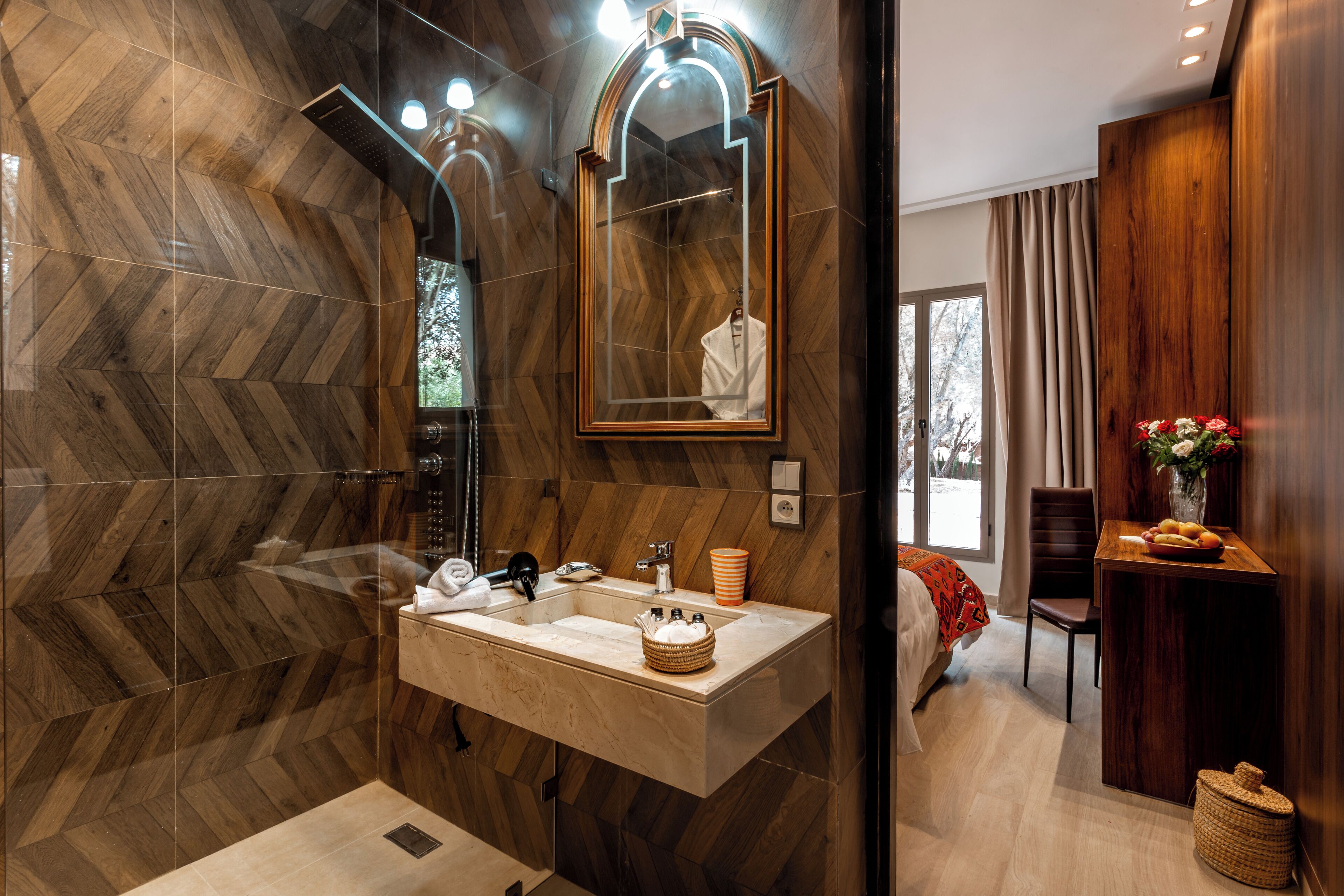 A modern bathroom with a herringbone wood floor, a large mirror, a sink with a vanity, and a shower.
