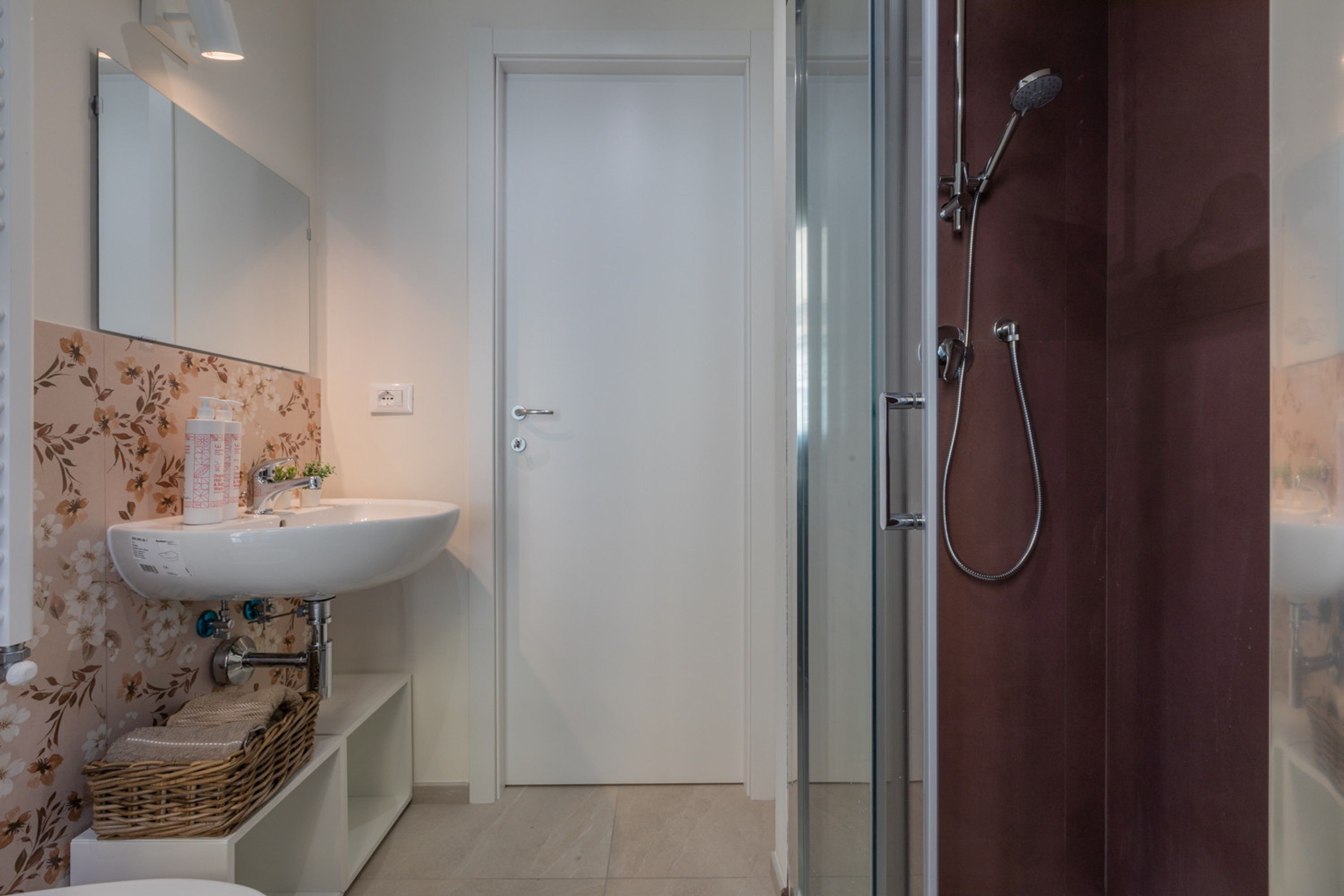 A bathroom with a white sink, a mirror, a shower, and a door.