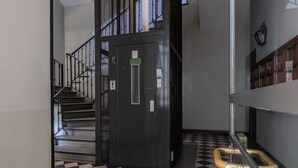 A hallway with a black and white checkered floor, a metal elevator, and a staircase with metal railings. - Ai Portici di Susa - Cozy by Wonderful Italy (Turin)