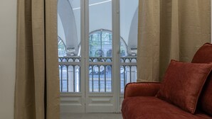 A room with a red sofa, a large window with a view of a street and buildings, and a white door with a glass panel. - Ai Portici di Susa - Cozy by Wonderful Italy (Turin)