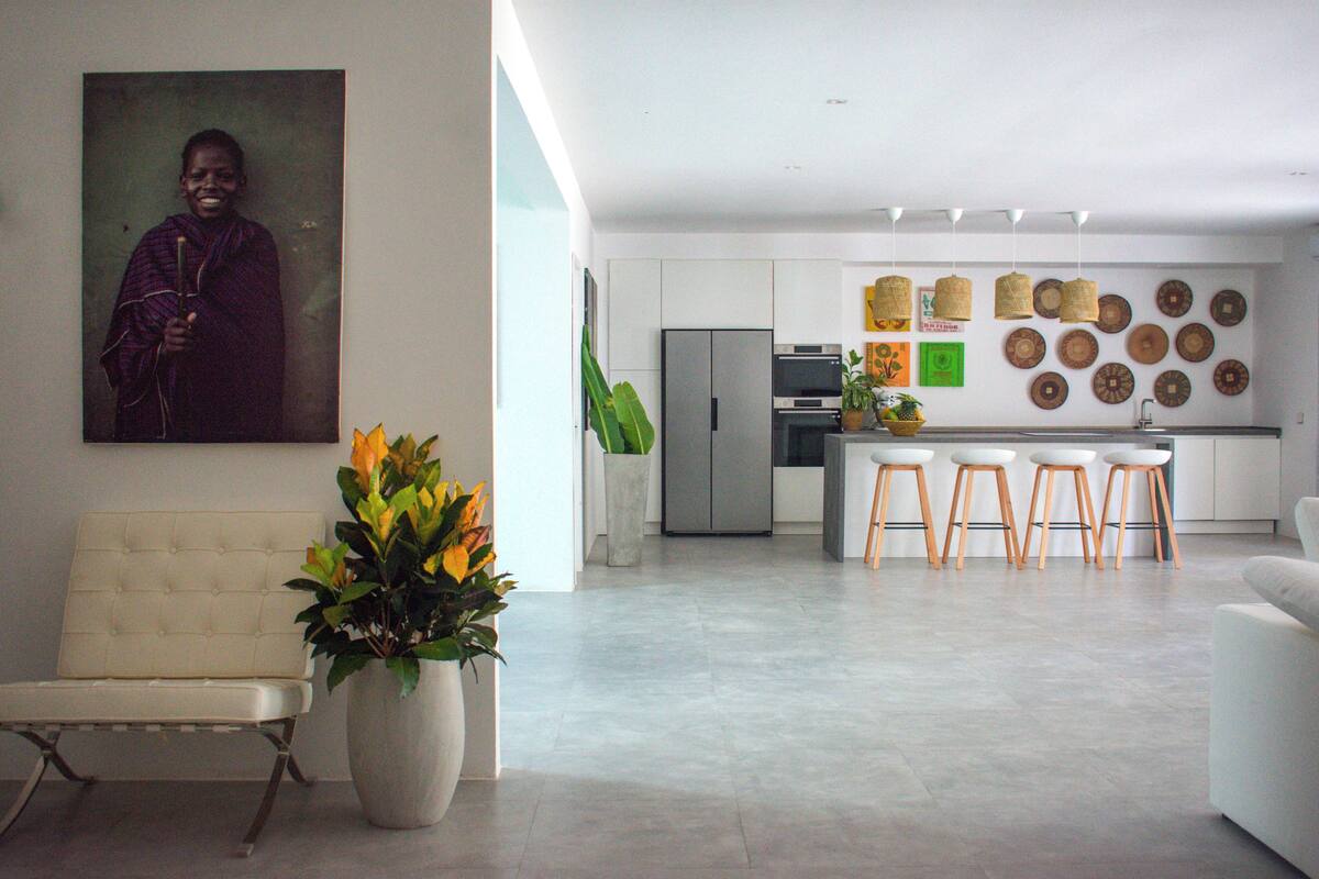 A modern kitchen with a central island, a dining area with bar stools, and a seating area with a sofa and a chair.
