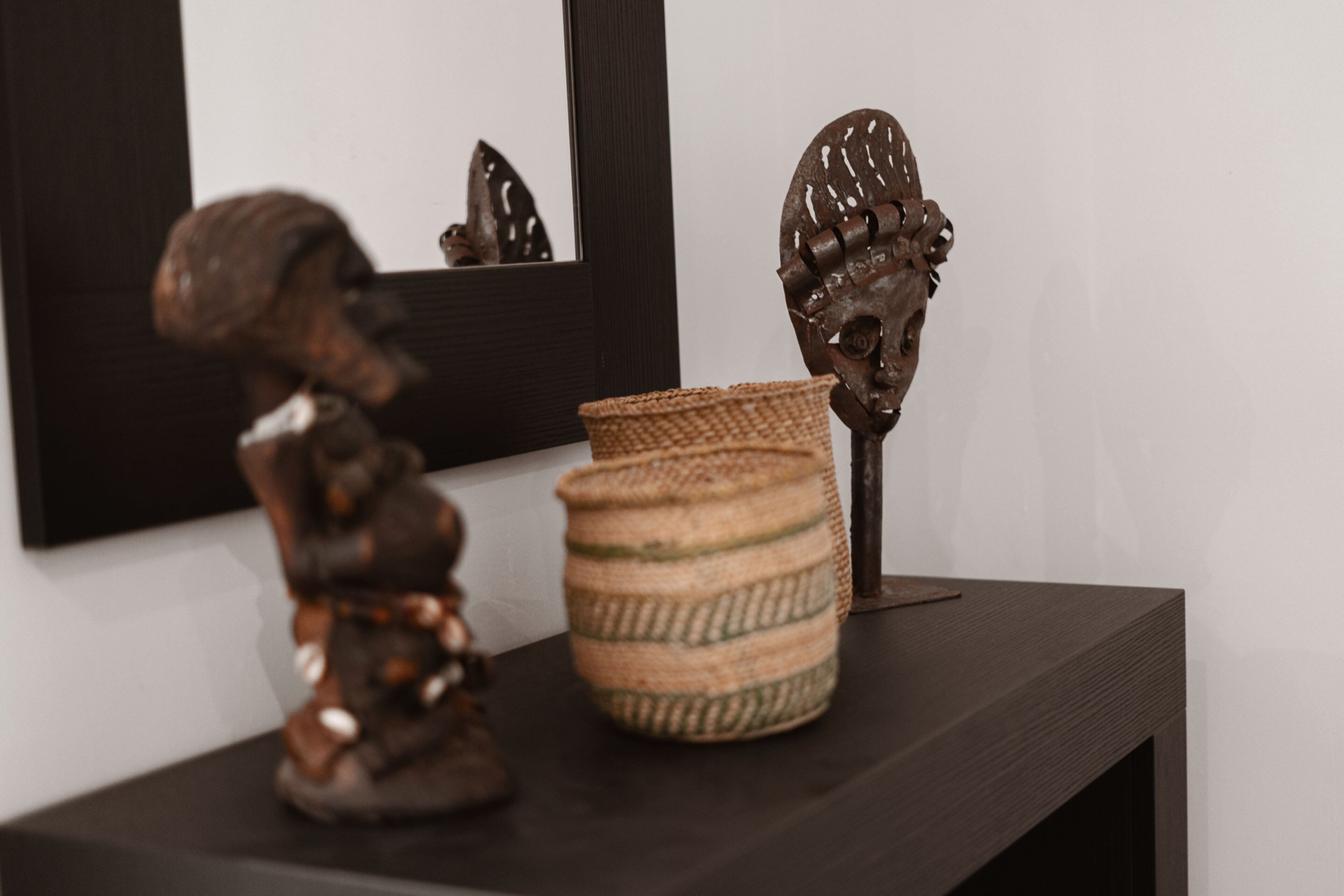 A small shelf with a sculpture, a woven basket, and a mirror.