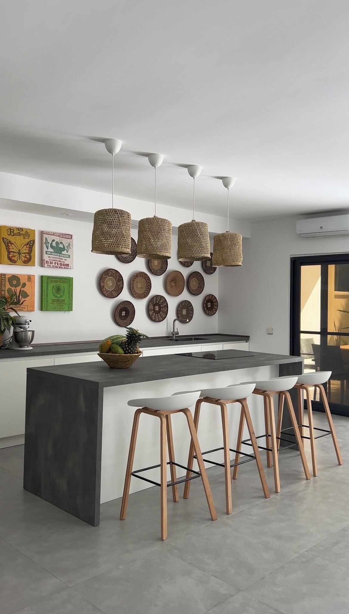 A modern kitchen with a central island, pendant lights, and a variety of decorative plates on the wall.