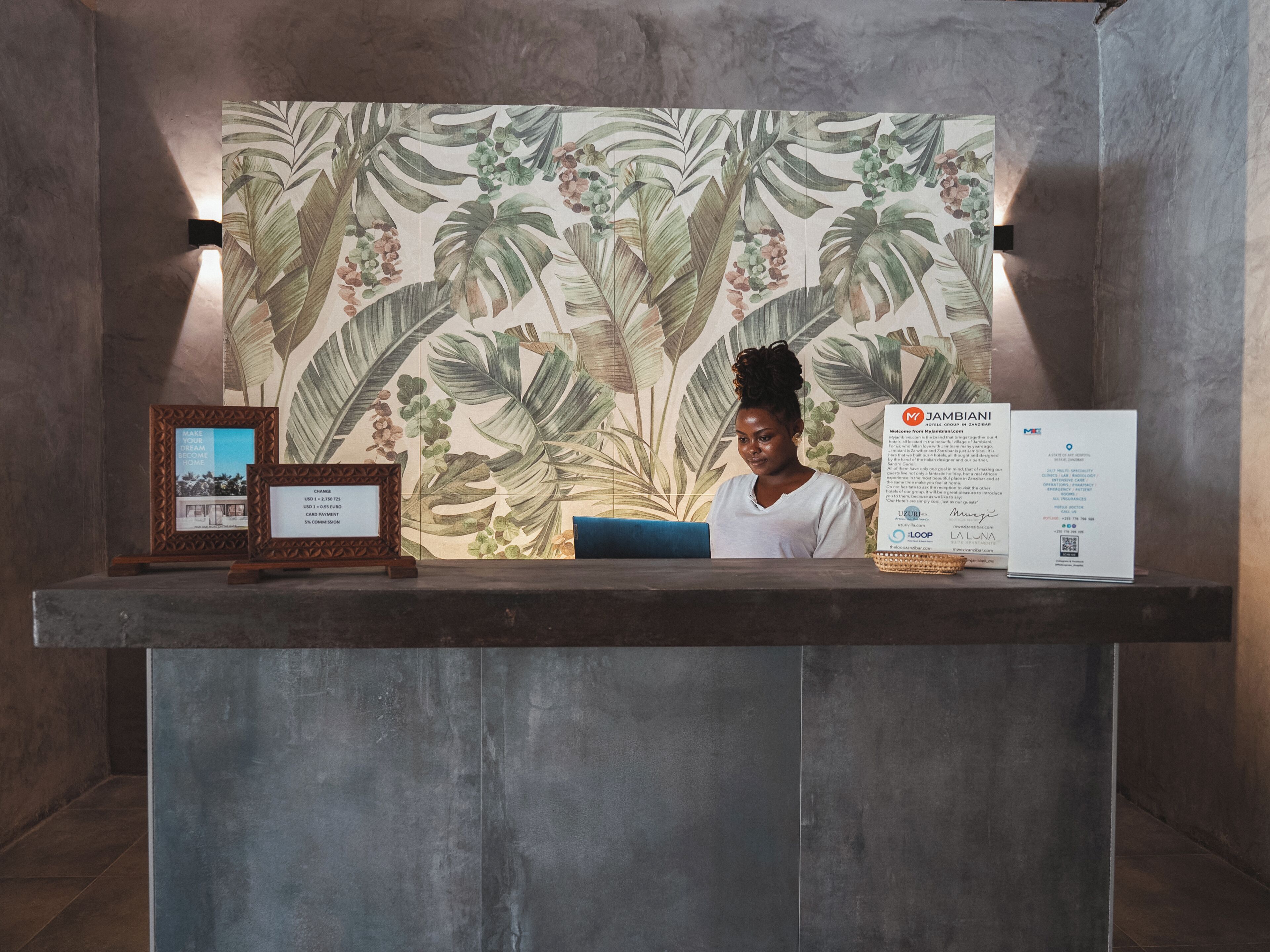 A reception desk with a tropical leaf pattern backdrop, framed pictures, and informational signs.
