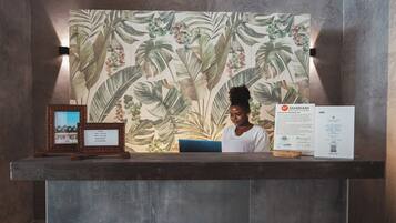 A reception desk with a tropical leaf pattern backdrop, framed pictures, and informational signs.