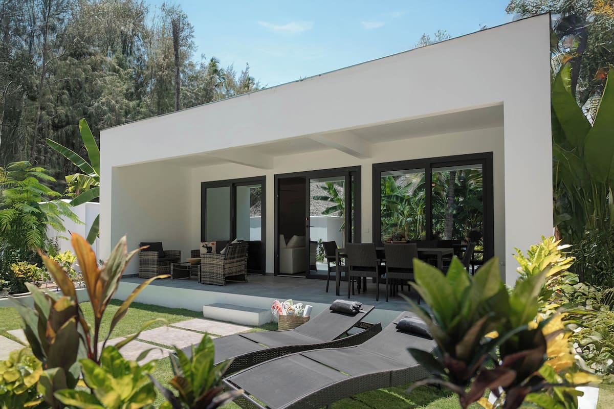 A modern outdoor patio with lounge chairs, a dining area, and a large window overlooking a garden.