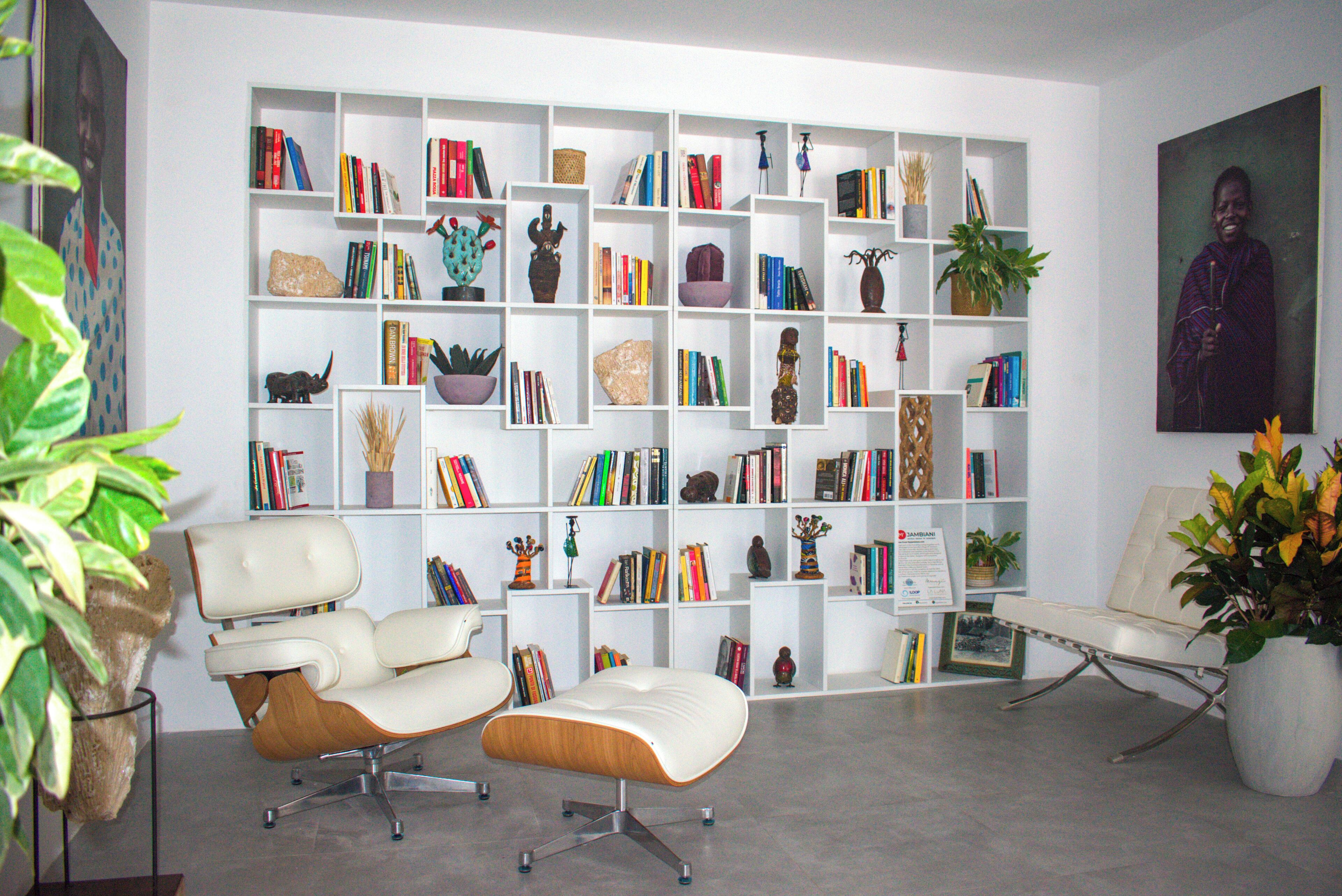 A modern living room with a white bookshelf filled with books and decorative items, a white leather sofa, and a coffee table.