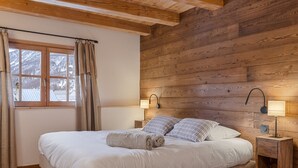 Une chambre confortable avec une tête de lit en bois, un grand lit avec du linge de lit blanc, deux lampes de chevet et une fenêtre avec des rideaux.
