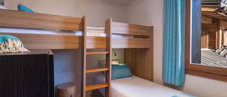 A bunk bed room with a desk, a lamp, and a window with curtains.