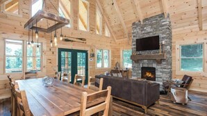A spacious cabin interior with a large wooden dining table, a stone fireplace, and a cozy seating area. - Coshocton Hills - 2 Luxury Log Cabins - Lake (West Lafayette)