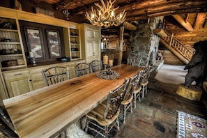 Un coin repas rustique avec une longue table et des chaises en bois, un lustre et un mur en pierre.
