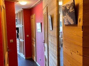 A hallway with red walls, wooden doors, and a framed picture on the wall.