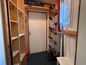 A narrow hallway with wooden shelves on the left, a door at the end, and a wall-mounted rack with tools on the right. - Charming apartment with sauna for 6 guests (Avoriaz)