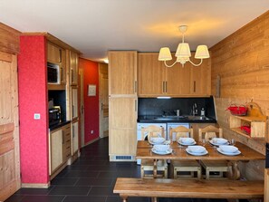 A modern kitchen with wooden cabinets, a dining table set for four, and a chandelier. - Charming apartment with sauna for 6 guests (Avoriaz)